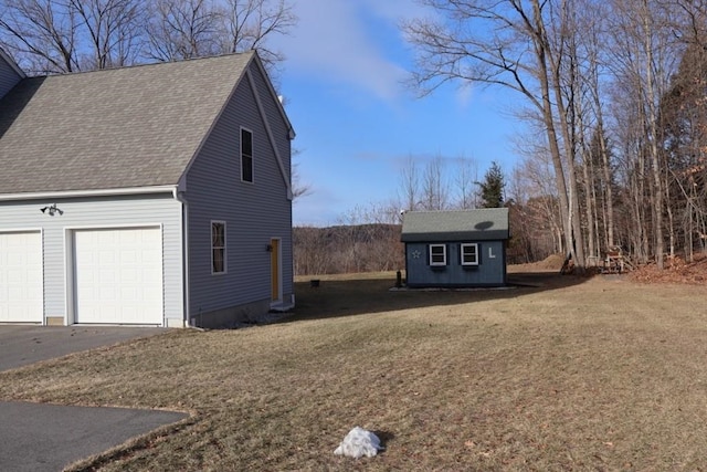 view of property exterior with a garage, a shingled roof, a yard, a storage unit, and an outdoor structure