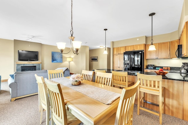 carpeted dining area with a tile fireplace and ceiling fan with notable chandelier