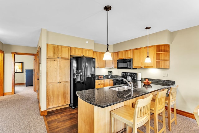 kitchen with kitchen peninsula, dark stone counters, sink, black appliances, and pendant lighting