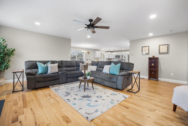 living room with light hardwood / wood-style floors and ceiling fan with notable chandelier