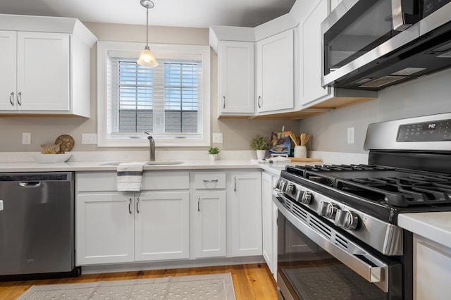 kitchen with white cabinetry, sink, hanging light fixtures, stainless steel appliances, and light wood-type flooring