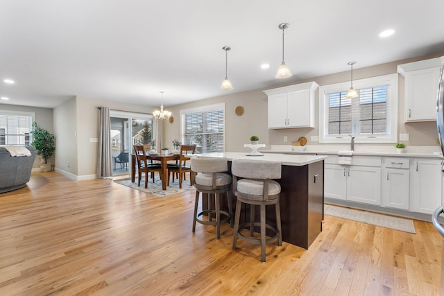 kitchen with white cabinetry, a kitchen island, hanging light fixtures, and light wood-type flooring