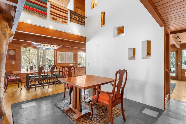 dining space with a wealth of natural light, beamed ceiling, a towering ceiling, and wood walls