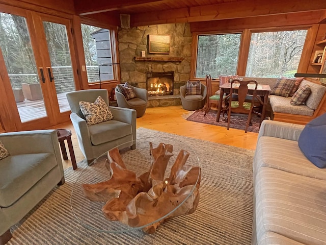 living room featuring french doors, wood ceiling, beam ceiling, light hardwood / wood-style floors, and a stone fireplace