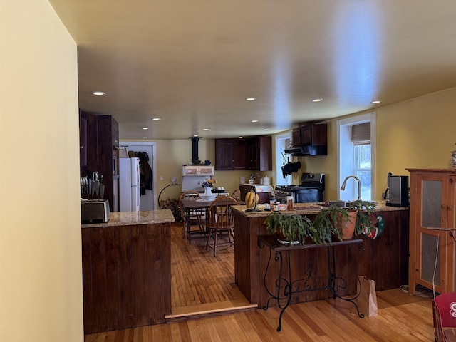 kitchen featuring kitchen peninsula, white fridge, light wood-type flooring, and stainless steel range with gas stovetop