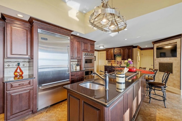 kitchen with decorative light fixtures, decorative backsplash, sink, appliances with stainless steel finishes, and an island with sink