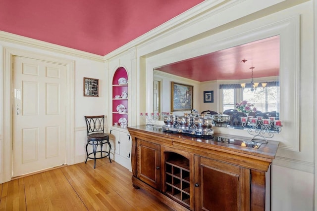 bar with decorative light fixtures, built in shelves, light hardwood / wood-style floors, ornamental molding, and a notable chandelier