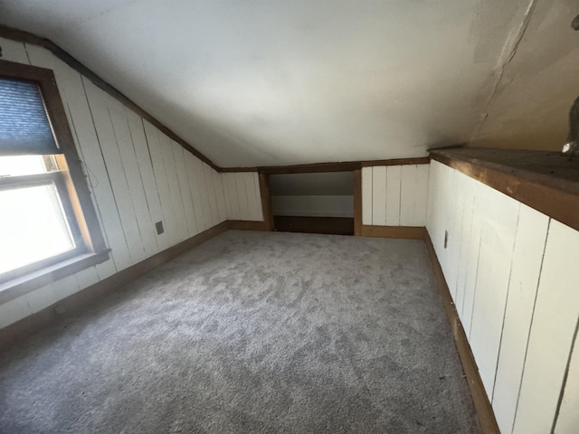 additional living space with dark colored carpet, radiator heating unit, wooden walls, and lofted ceiling