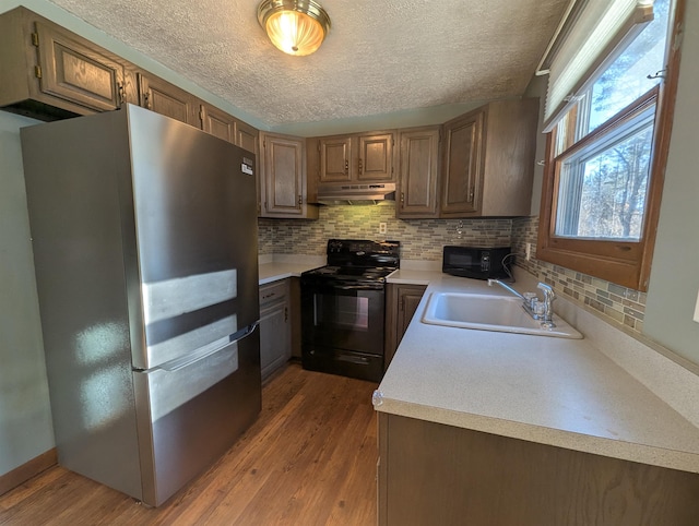 kitchen with black appliances, backsplash, sink, and hardwood / wood-style floors