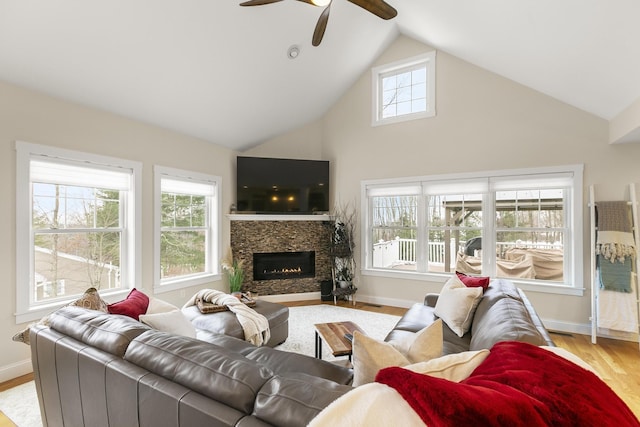 living room featuring plenty of natural light, ceiling fan, a stone fireplace, and light hardwood / wood-style floors