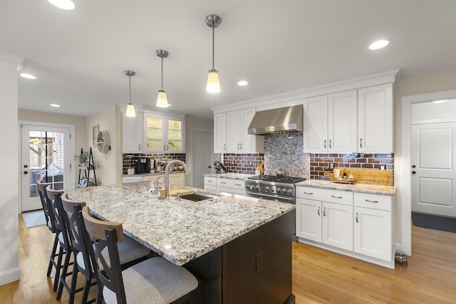 kitchen with white cabinets, wall chimney exhaust hood, sink, and hanging light fixtures