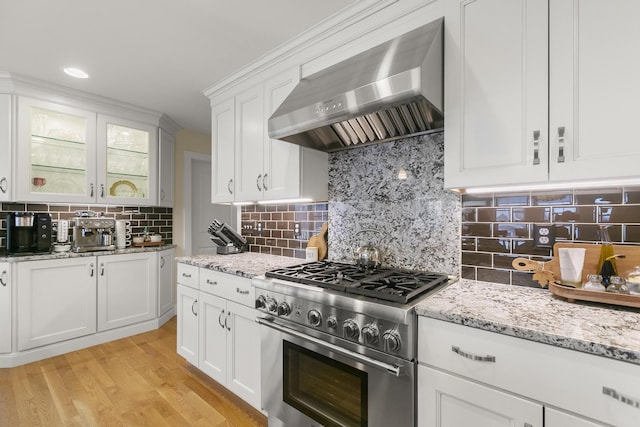 kitchen featuring white cabinets, wall chimney range hood, stainless steel range, tasteful backsplash, and light hardwood / wood-style floors