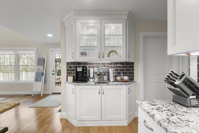 bar featuring decorative backsplash, light hardwood / wood-style flooring, white cabinetry, and light stone counters