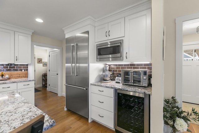 kitchen featuring white cabinets, built in appliances, decorative backsplash, light wood-type flooring, and beverage cooler