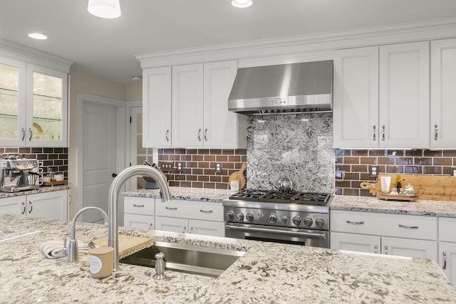 kitchen with white cabinetry, wall chimney range hood, backsplash, and stainless steel stove