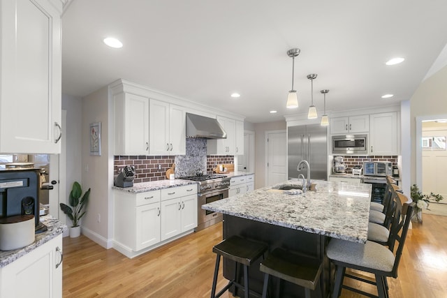 kitchen featuring decorative backsplash, sink, wall chimney range hood, built in appliances, and white cabinets