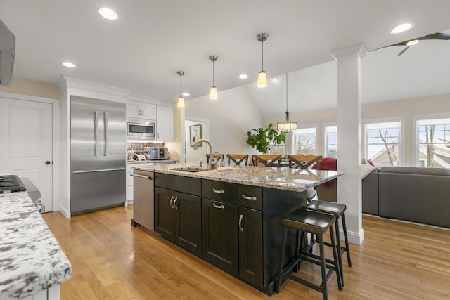 kitchen with light stone countertops, sink, built in appliances, white cabinetry, and an island with sink