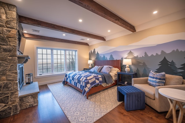 bedroom featuring beamed ceiling, a stone fireplace, and hardwood / wood-style floors