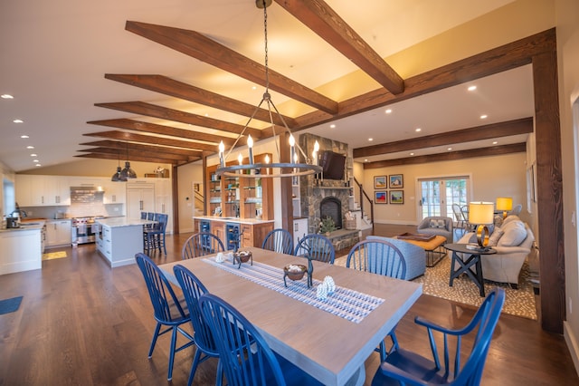 dining area featuring sink, vaulted ceiling with beams, dark hardwood / wood-style floors, a notable chandelier, and a stone fireplace