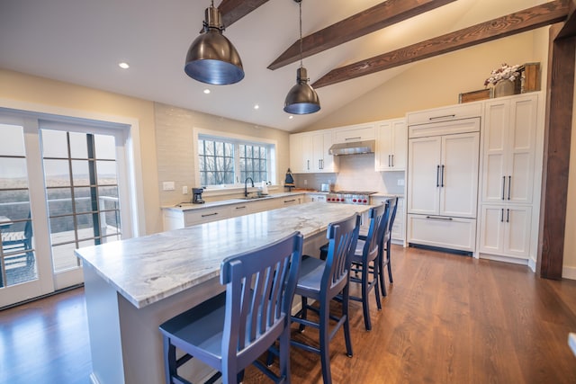 kitchen featuring white cabinetry, a center island, paneled built in fridge, pendant lighting, and light stone countertops