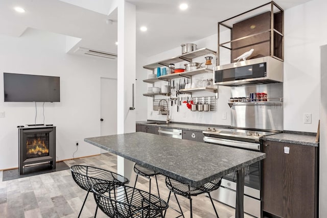 kitchen with a kitchen breakfast bar, sink, light hardwood / wood-style flooring, appliances with stainless steel finishes, and dark brown cabinets