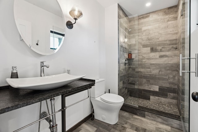 bathroom with hardwood / wood-style floors, vanity, toilet, and a shower with door