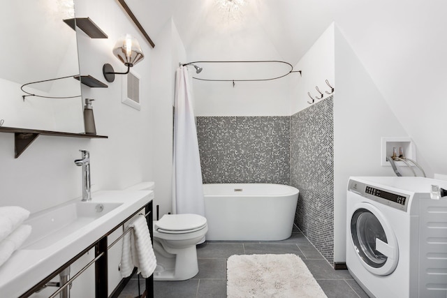 bathroom featuring a bathing tub, sink, washer / dryer, tile patterned floors, and toilet