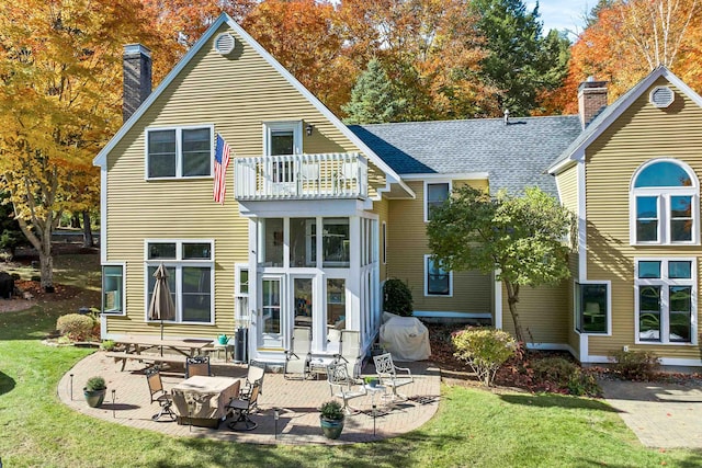 rear view of house featuring a lawn, a balcony, and a patio