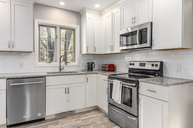 kitchen featuring white cabinetry, sink, light stone countertops, backsplash, and appliances with stainless steel finishes