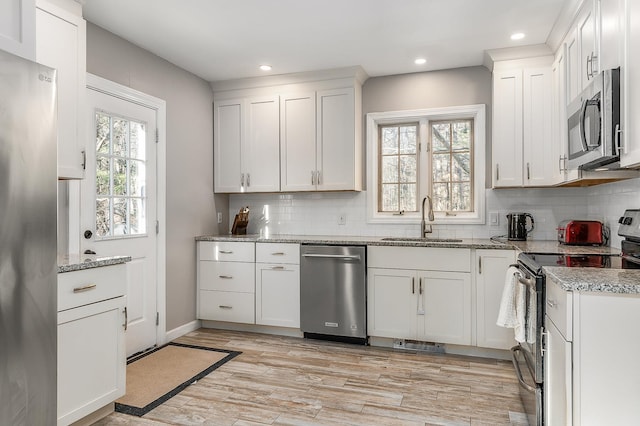 kitchen with sink, decorative backsplash, appliances with stainless steel finishes, light hardwood / wood-style floors, and white cabinetry