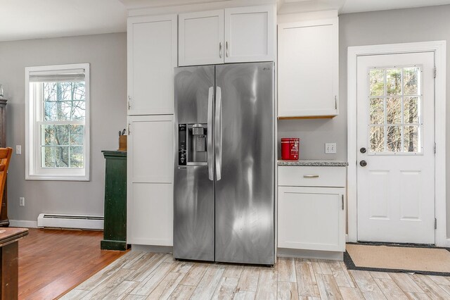 kitchen featuring white cabinets, stainless steel fridge, light stone countertops, light wood-type flooring, and a baseboard radiator