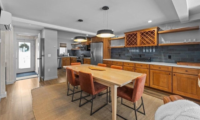 kitchen featuring appliances with stainless steel finishes, tasteful backsplash, an AC wall unit, light hardwood / wood-style floors, and hanging light fixtures