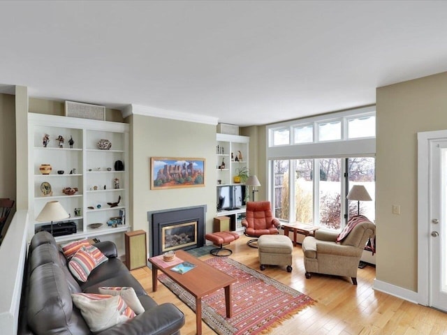 living area featuring a glass covered fireplace, baseboards, and light wood finished floors