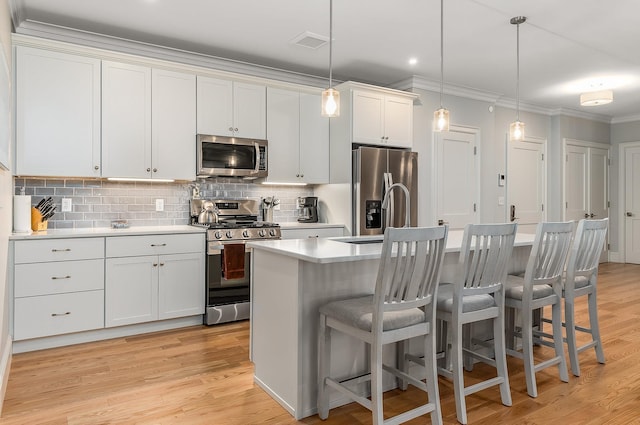 kitchen featuring hanging light fixtures, tasteful backsplash, a kitchen island with sink, white cabinets, and appliances with stainless steel finishes