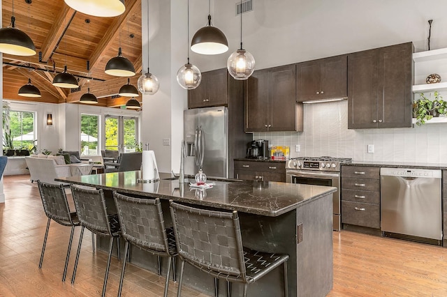 kitchen with beam ceiling, stainless steel appliances, dark stone counters, a kitchen bar, and wood ceiling