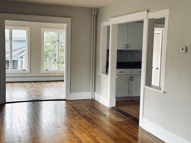 unfurnished room with dark hardwood / wood-style flooring and a baseboard heating unit