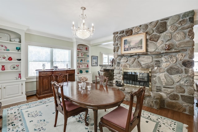 dining area with a baseboard heating unit, a stone fireplace, crown molding, built in features, and wood-type flooring