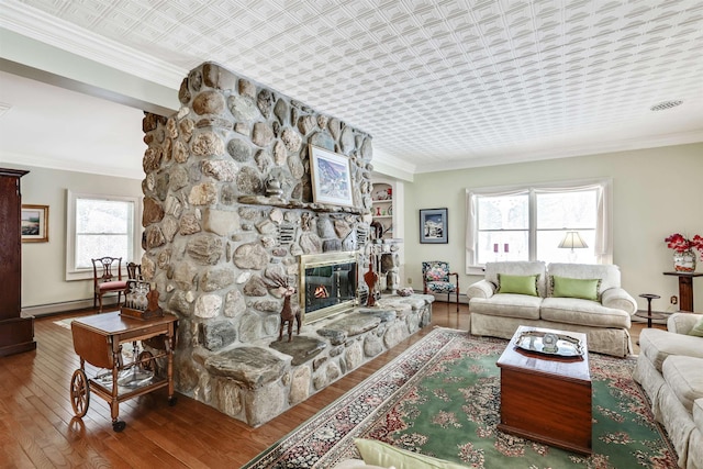 living room featuring baseboard heating, a stone fireplace, wood-type flooring, and ornamental molding