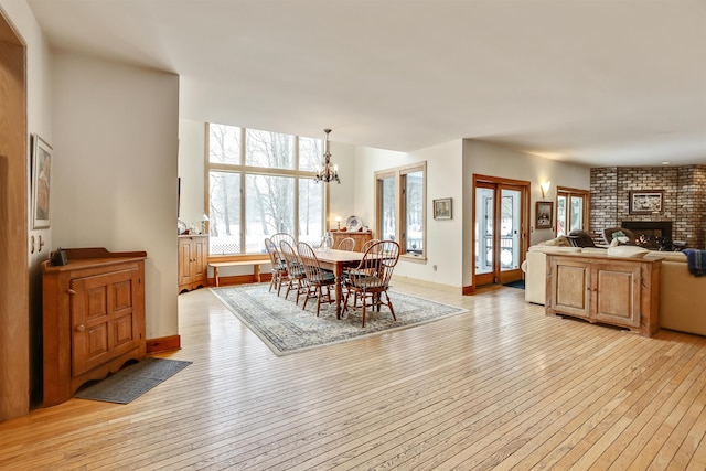 dining area with a notable chandelier, light wood-type flooring, and a brick fireplace