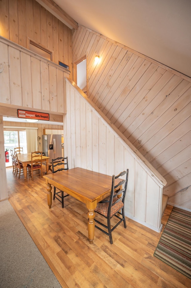 dining room featuring lofted ceiling, wooden walls, and light hardwood / wood-style flooring