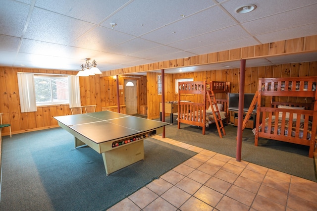 playroom with tile patterned flooring, a drop ceiling, and wood walls