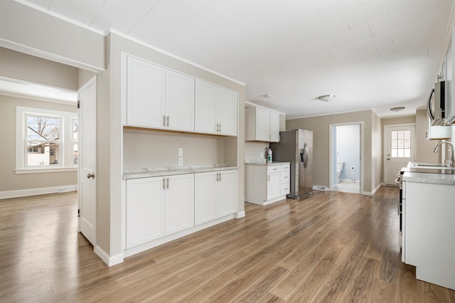 kitchen featuring appliances with stainless steel finishes, ornamental molding, sink, white cabinets, and light hardwood / wood-style floors