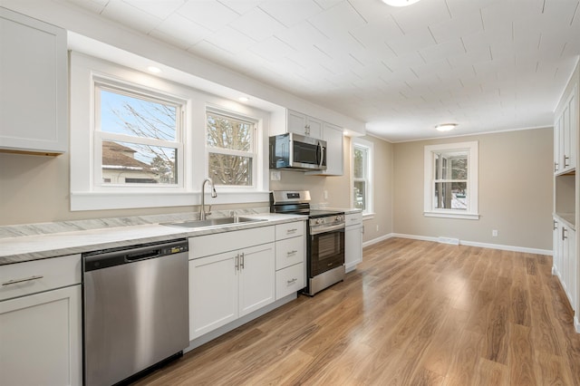 kitchen with appliances with stainless steel finishes, light wood-type flooring, light stone counters, sink, and white cabinets