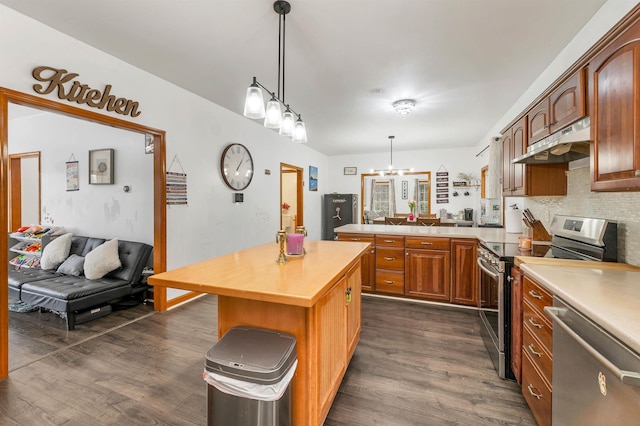 kitchen featuring appliances with stainless steel finishes, decorative light fixtures, a kitchen island, and dark wood-type flooring