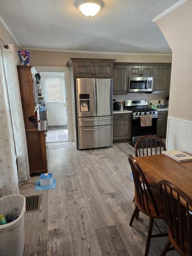 kitchen with stainless steel appliances, dark brown cabinets, light hardwood / wood-style floors, and crown molding