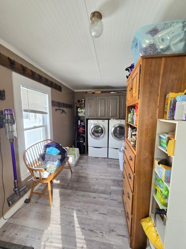 clothes washing area with cabinets, washing machine and clothes dryer, and light hardwood / wood-style floors