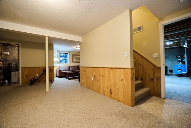 corridor featuring a textured ceiling, light colored carpet, and wooden walls