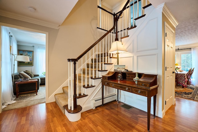 stairway featuring wood-type flooring, ornamental molding, and a baseboard heating unit