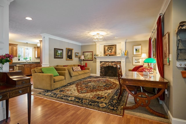 living room featuring light wood-type flooring, ornamental molding, a textured ceiling, sink, and a fireplace