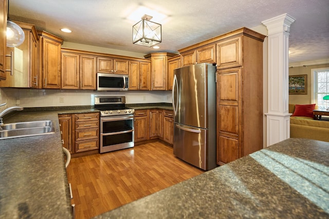 kitchen with sink, stainless steel appliances, decorative columns, decorative light fixtures, and light wood-type flooring